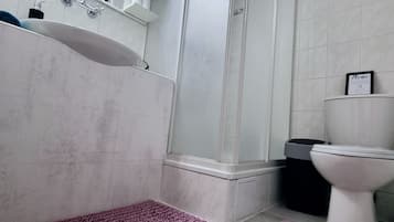 Un baño con lavamanos, espejo, ducha, inodoro y una alfombra morada.