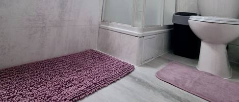 A bathroom with a sink, mirror, shower, toilet, and a purple rug.