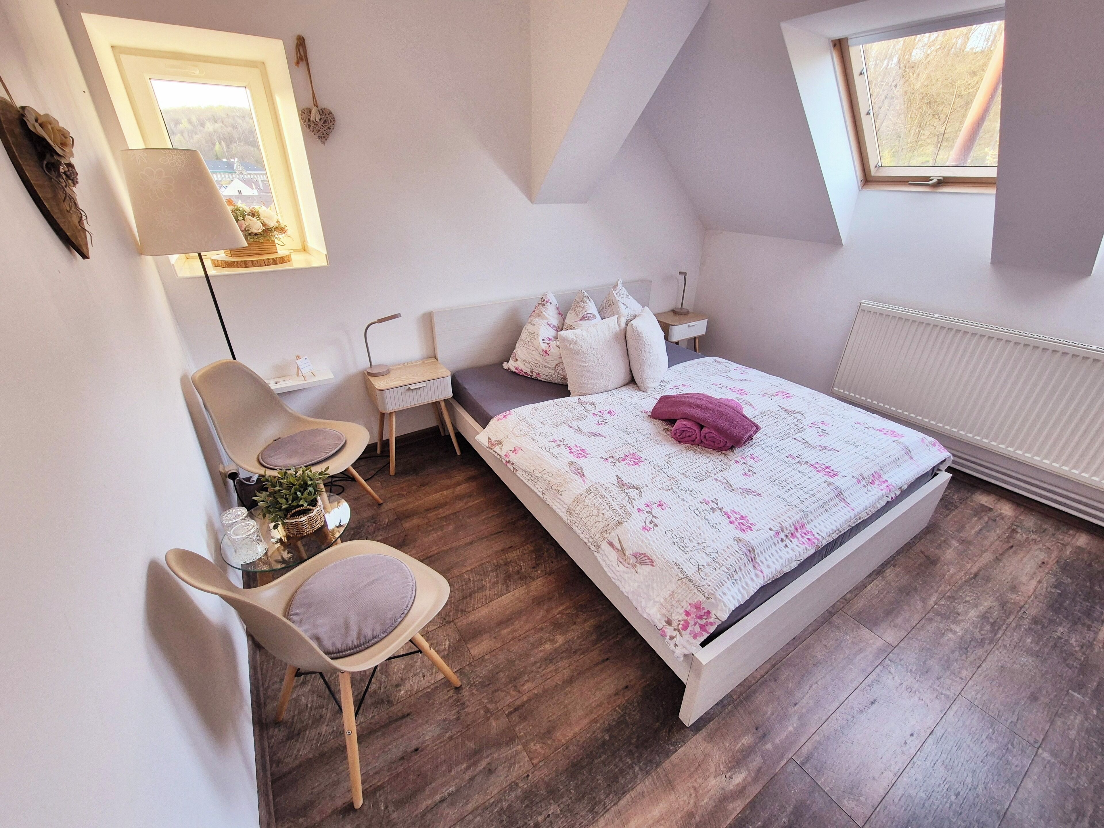 A bedroom with a bed, a chair, a nightstand, a lamp, and a window.