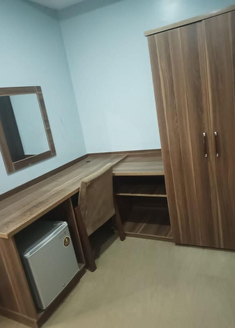 A corner room with a wooden desk, a wardrobe, and a small cabinet.