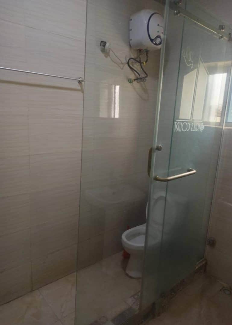 A glass-enclosed shower stall with a toilet and a wall-mounted water heater.
