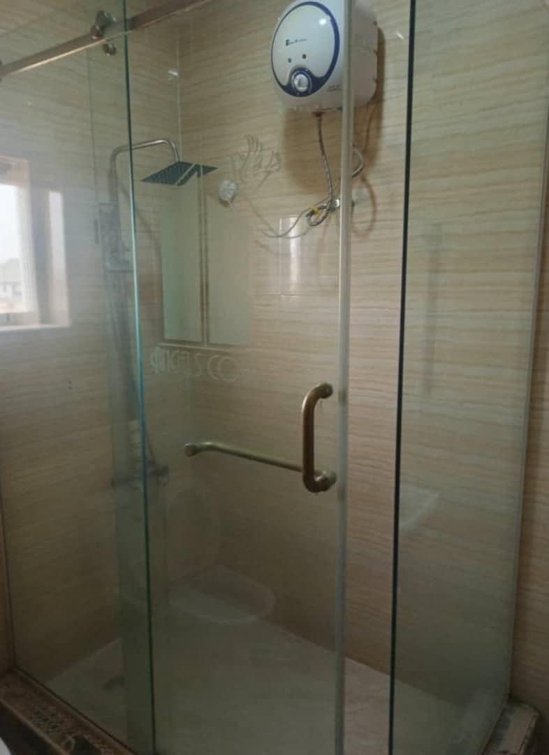 A glass-enclosed shower stall with a control panel, a handrail, and a tiled wall.