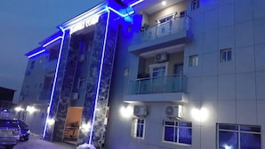 A multi-story building with balconies, air conditioning units, and a car parked in front. - Angels Court Hotel and Suite (Abuja)
