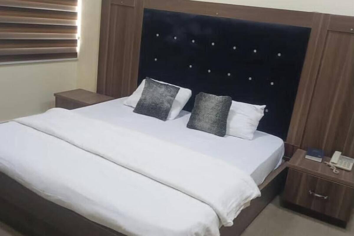 A neatly made bed with a dark headboard, two bedside tables, and a wall-mounted light fixture.