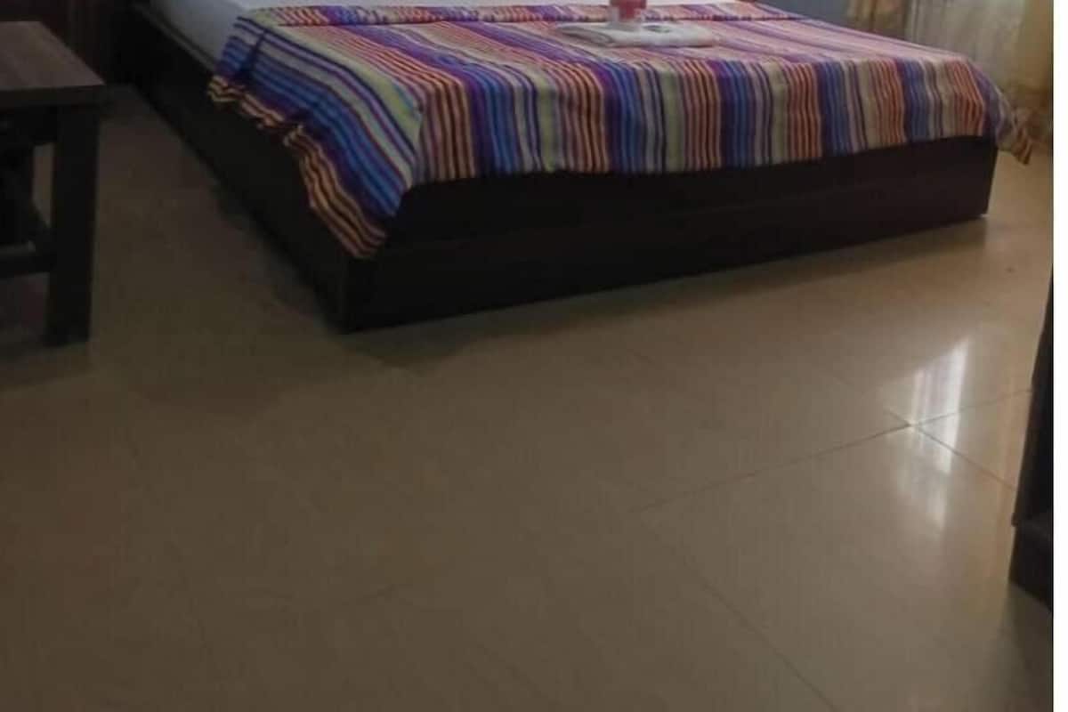 A hotel room with a large bed, a wooden headboard, a bedside table, and an air conditioning unit.