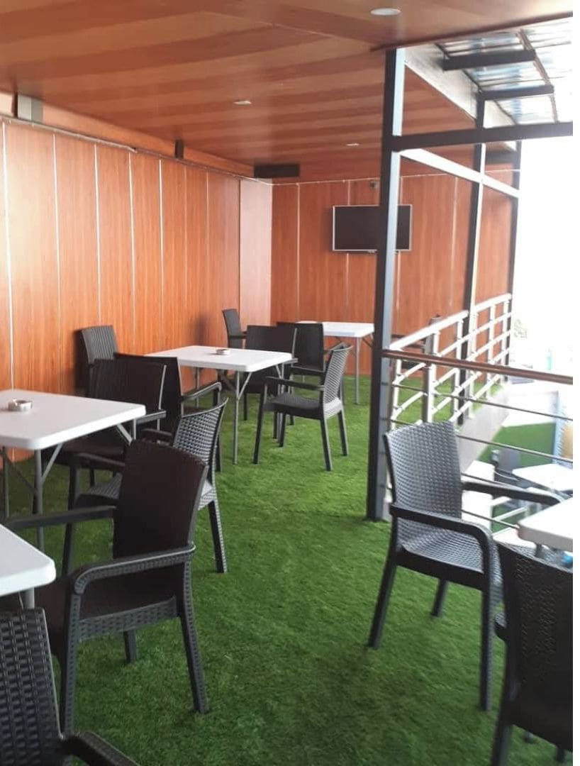 An outdoor seating area with tables and chairs, a wooden ceiling, and a view of a building in the background.