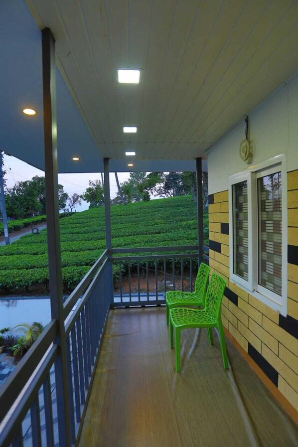 A balcony with a wooden floor, a green chair, and a view of a green tea plantation.