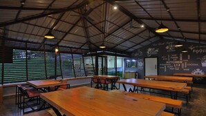 A spacious indoor dining area with wooden tables and benches, large windows with blinds, and a high ceiling with exposed beams. - The Svarga Hill View Resort (Devikolam)