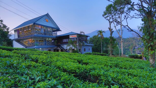 A two-story building with a balcony, surrounded by lush green tea plantations. - The Svarga Hill View Resort (Devikolam)