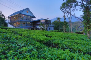 A two-story building with a balcony, surrounded by lush green tea plantations.