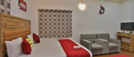 A bedroom with a bed, a grey sofa, a TV, and a wooden desk.