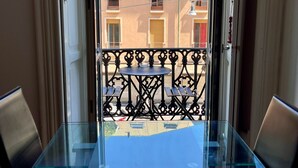 Een balkon met een glazen tafel en stoelen, met uitzicht op een gebouw met meerdere balkons en ramen.