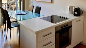 Een kleine keuken met een glazen eettafel, een inbouwfornuis en een groot raam met uitzicht op een gebouw.