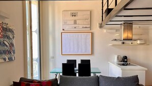 Een moderne woonkamer met een grijze bank, een eettafel met stoelen en een keuken met fornuis en spoelbak.