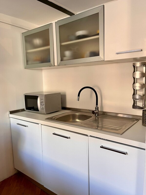 A compact kitchen with a microwave, sink, and cabinets.