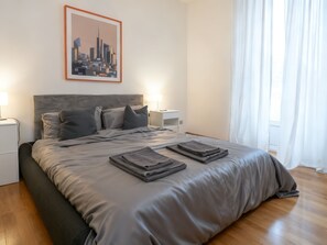 Un dormitorio moderno con una cama grande, un cuadro de un paisaje urbano en la pared y una mesita de noche con una lámpara.