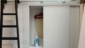 Une armoire blanche avec un fer à repasser suspendu et un cintre rouge.