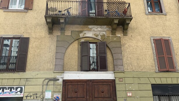 Un bâtiment doté d’une grande porte d’entrée en bois à deux battants, de nombreuses fenêtres avec volets et d’un petit balcon orné d’une rambarde en métal.