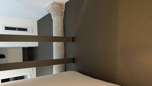 Une pièce avec un lit superposé, un mur gris et un pilier en pierre.