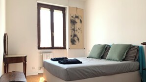 A bedroom with a bed, a wooden chest, a radiator, a window, and a painting on the wall. - Bright & Pop Flat Isola & Central Station Hub (Milan)