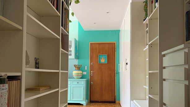 A hallway with open shelving on both sides, a wooden door with a crown symbol, and a light blue cabinet. - Bright & Pop Flat Isola & Central Station Hub (Milan)