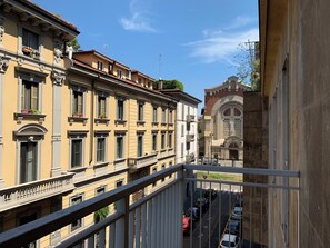 Vista da un balcone su una strada con auto parcheggiate e edifici storici dall'architettura classica.