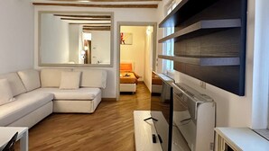 Una sala de estar moderna con un sofá blanco, piso de madera, un espejo grande y una estantería empotrada para la televisión.
