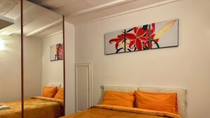 Una habitación de hotel con dos camas, cada una con ropa de cama naranja y toallas blancas. Hay un espejo grande en una pared y un cuadro de flores sobre las camas.