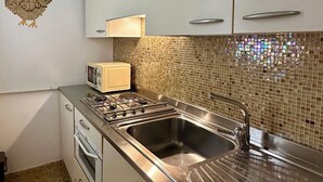Una cocina con armarios blancos, salpicadero de azulejos, pileta de acero inoxidable y un tostador.