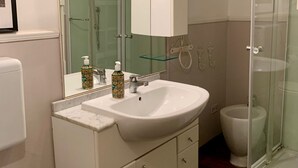 Une salle de bain moderne avec un meuble-lavabo blanc, un grand miroir, une douche en verre et des toilettes.