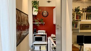 Un couloir étroit avec un coin cuisine comprenant un four à micro-ondes, une horloge et des étagères avec des plantes.