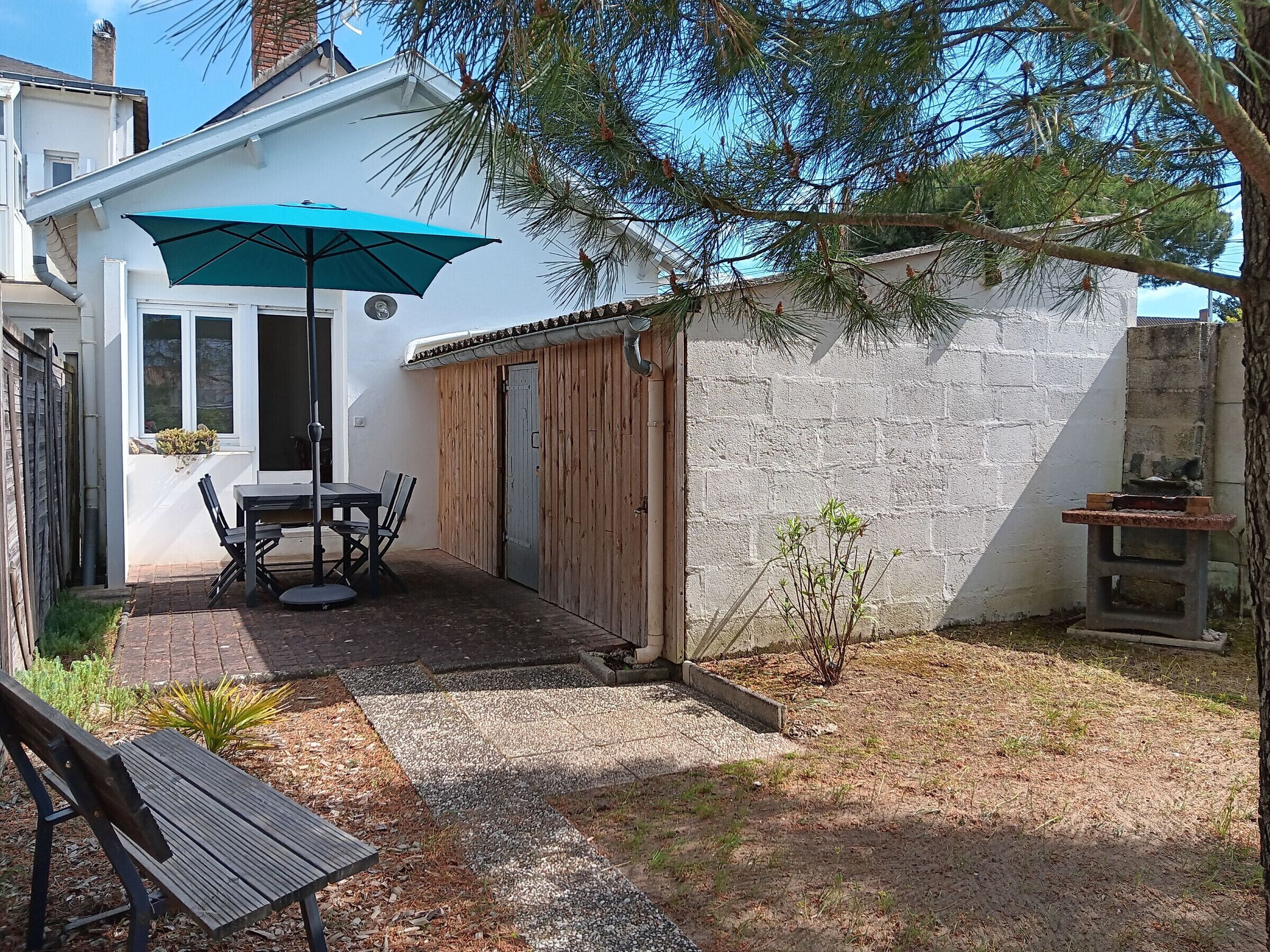 A patio with a table and chairs, a wooden fence, a small plant, and a building with a tiled roof.