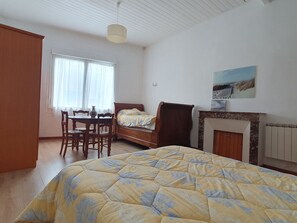 A bedroom with a bed, a dining table with chairs, a fireplace, and a painting on the wall.
