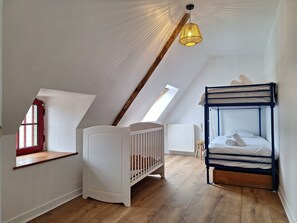 Une pièce aux hauts plafonds, avec un plafond en pente, un berceau, un lit superposé et une lucarne.