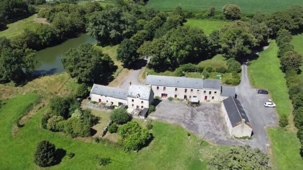An aerial view of a large, rectangular building with a central courtyard, surrounded by lush greenery and a river.