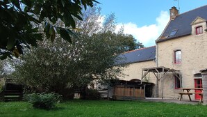 A stone building with a wooden porch, a picnic table, and a small shed.