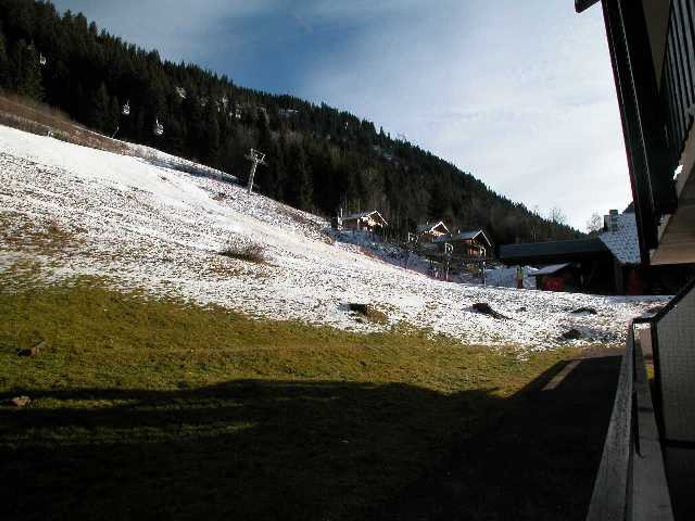 Un paysage enneigé avec quelques maisons et une colline boisée en arrière-plan.