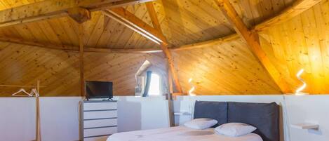 A bedroom with a sloped wooden ceiling, a bed, a dresser, and a television.