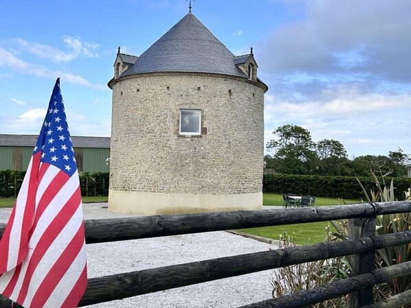 Une tour de pierre surmontée d’un toit conique, avec une petite fenêtre et un drapeau américain en premier plan.