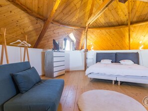Une chambre mansardée chaleureuse avec un plafond en bois, un lit, un canapé et une commode.