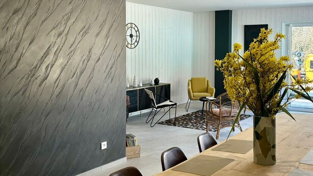 A modern dining area with a marble wall, a dining table, chairs, a yellow armchair, and a vase with yellow flowers. - Spacious lodge in Sanchey near the lake, sauna, games, close to nature (Sanchey)