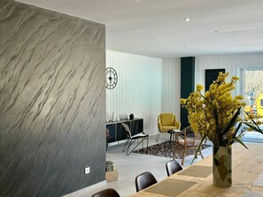 A modern dining area with a marble wall, a dining table, chairs, a yellow armchair, and a vase with yellow flowers. - Spacious lodge in Sanchey near the lake, sauna, games, close to nature (Sanchey)