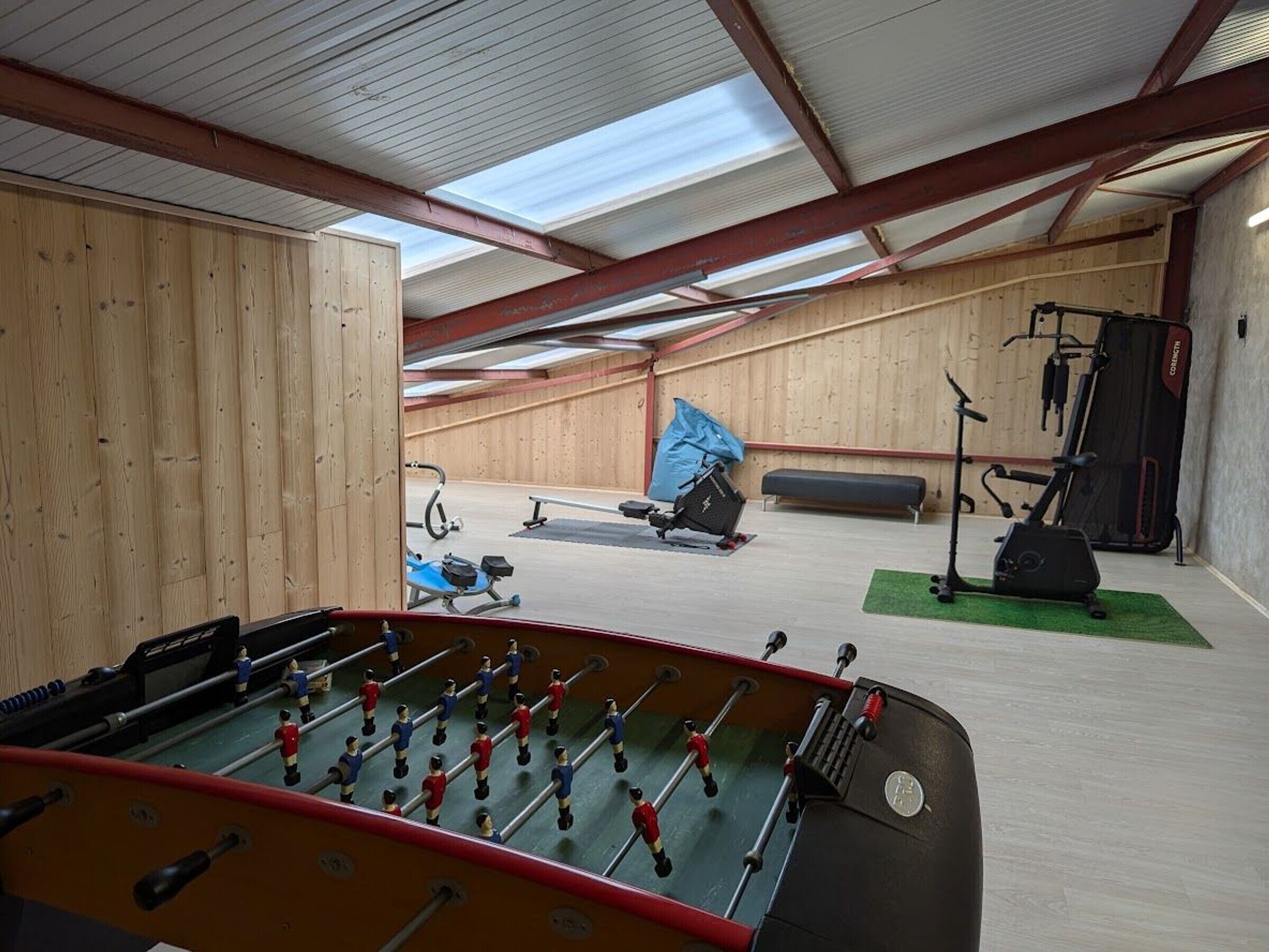 Un grand espace intérieur comprenant une table de baby-foot, du matériel d’exercice et un banc.