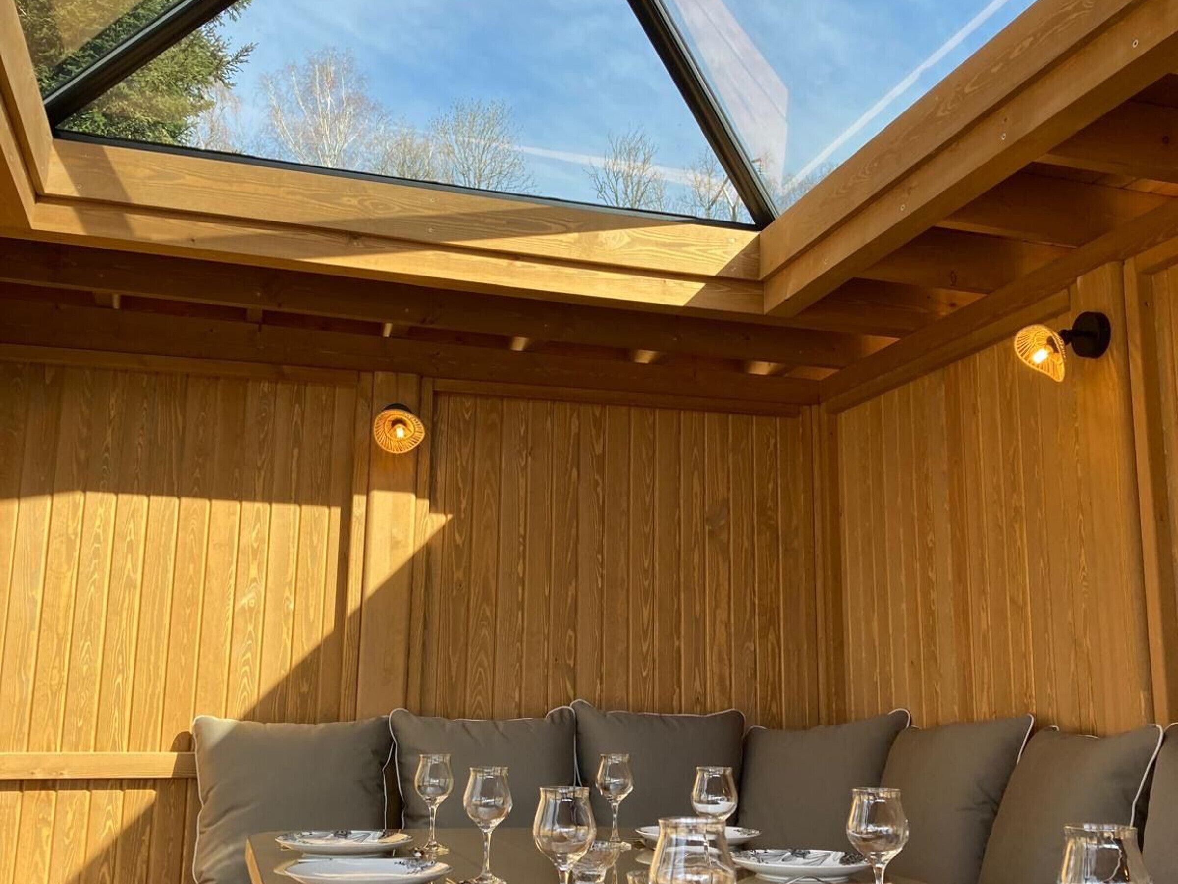 A wooden interior with a table set for dining, a skylight, and a wall-mounted light fixture.