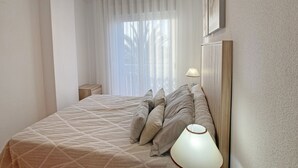 Un dormitorio con cama, mesita de noche, lámpara y ventana con cortinas.