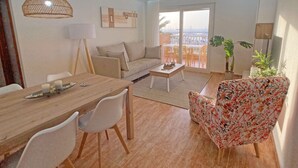 Una sala de estar moderna con sofá, mesa de centro, mesa de comedor con sillas y un balcón con mobiliario exterior.