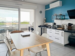 A modern kitchen with white cabinets, a black countertop, and a view of the city through large windows. - Charming PMR apartment with terrace, air conditioning and parking in Palavas (Palavas-les-Flots)