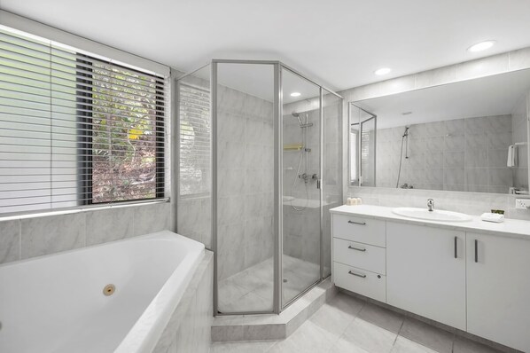 Uma casa de banho moderna com chuveiro em cabine de vidro, banheira e toucador com espelho.