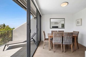 A balcony with a glass door, a dining table with wicker chairs, a ceiling light, and a framed picture on the wall.