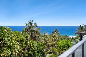 Uma varanda com vista para o oceano e vegetação tropical.